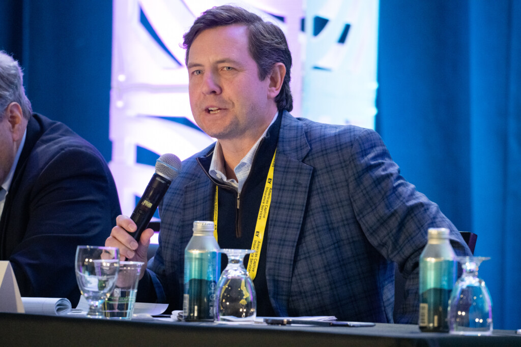 A speaker in a blue plaid jacket holds a microphone and speaks at the CICA 2026 International Conference